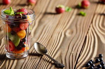 Assorted berries in mason jar on kitchen wooden table with spoon aside