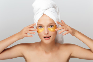 Portrait of young pretty lady with white towel on head without makeup with yellow patches under eyes dreamily looking in camera over gray background isolated