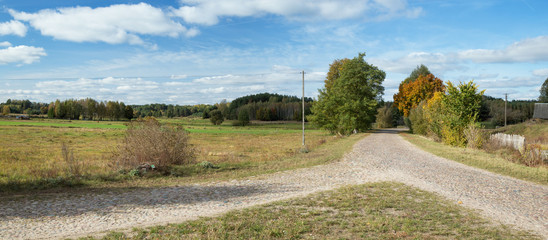 Crossing the old stone country road, you can see fields, a fence, a pillar and a nice blue sky with...