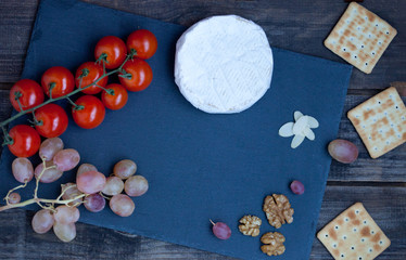 Camembert cheese on a black stone plate with tomatoes, crackers, nuts and grape