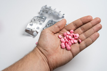 Mans hands with pills on, spilling pills out of bottle on white background