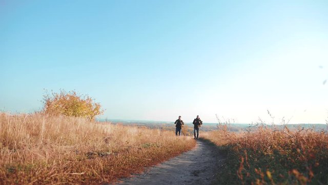 Two men lifestyle traveler hiking with backpacks are walking along the path climbing into the mountains. slow motion video. Tourist Hipster Hiker traveler on background view blue sky clouds go hiking