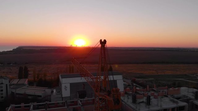Construction site with a bird's eye on the Sunset. Video shooting with drone. Tower crane, excavator and sand. Flying over the construction site. The construction of the plant in the city.