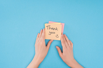 cropped person holding colorful sticky notes with thank you lettering isolated on blue background