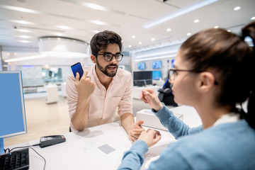 Man standing on cashier and complaining for new smart phone while worker listening to him. Tech...