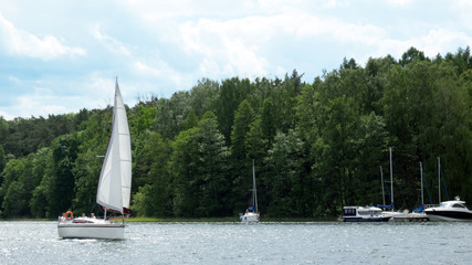 White boat sailing on the lake near Mikolajki, Poland under a cloudy sky. 
