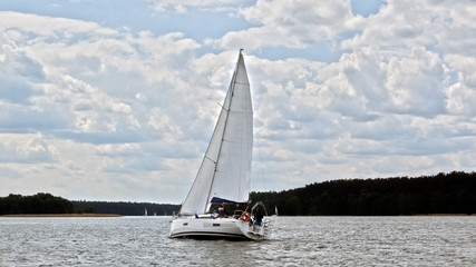 Obraz premium White boat sailing on the lake near Mikolajki, Poland under a cloudy sky. 
