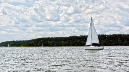 White boat sailing on the lake near Mikolajki, Poland under a cloudy sky. 