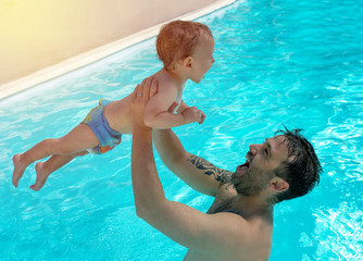 Father and child are having fun in pool. Dad and son are swimming indoor pool. Father teachs son to swim. Concept of kids sport, family summer vacation. Concept of healthy holiday and family activity.