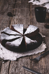 Kladdkaka. Traditional Swedish moist chocolate cake on old rustic wooden table decorated dry twigs, pine cones and birch bark. Fika. Hygge. Toned image