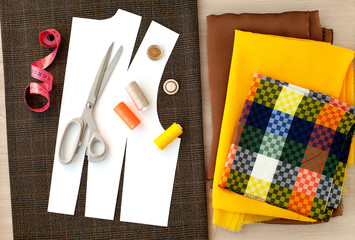 Sew clothes from stylish fabric. View from above. Paper pattern, checkered fabric, yellow and brown silk, measuring tape, tailoring scissors for sewing clothes. Fashion and dress design.
