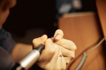 Girl handles nails with a milling cutter for manicure. Close up