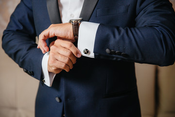 Close-up man puts on a gold watch with a leather belt, businessman is dressed in a stylish suit, a white shirt.