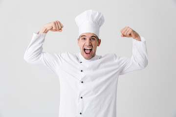 Excited young man chef indoors isolated over white wall background showing biceps.