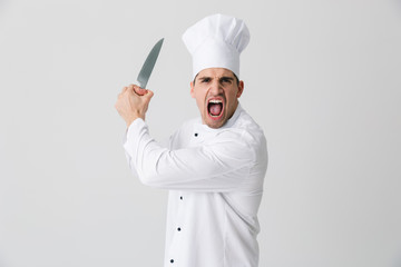 Agressive screaming young man chef indoors isolated over white wall background holding knife.