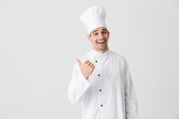Excited young man chef indoors isolated over white wall background pointing.