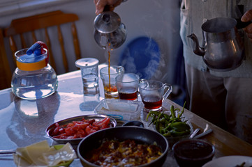 Hands of senior man with metal Turkish teapot pouring tea into glass cups for breakfast. Old Turkish man pouring tea.