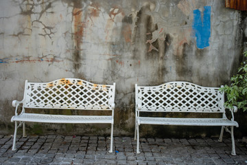 Couple of old metal chairs in front of old concrete wall with tiled floor.
