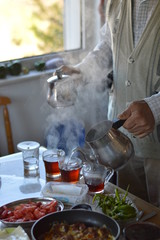 Hands of senior man with metal Turkish teapot pouring tea into glass cups for breakfast. Old Turkish man pouring tea.