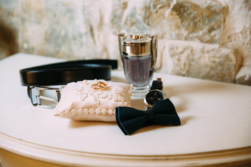 Men's accessories, leather belt, perfume, bow tie, groom's golden rings, watches and brides on a white table. Businessman clothing detail concept.