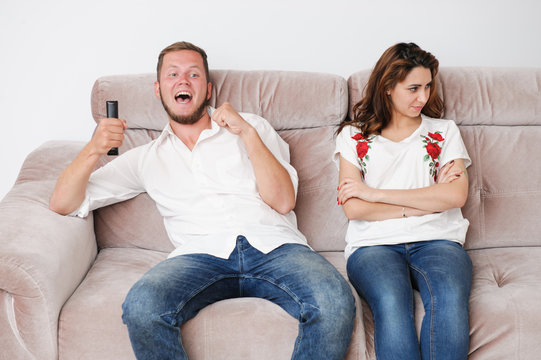 happy delightful football fan man with TV remote control and upset young woman