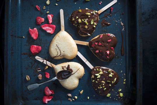 Heart shaped vegan cakes on sticks, decorated with a dark beer glaze, freeze-dried strawberries and pistachios