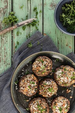 Portobello mushrooms stuffed with parmesan pine nuts garlic breadcrumbs and parsley on a green wooden table