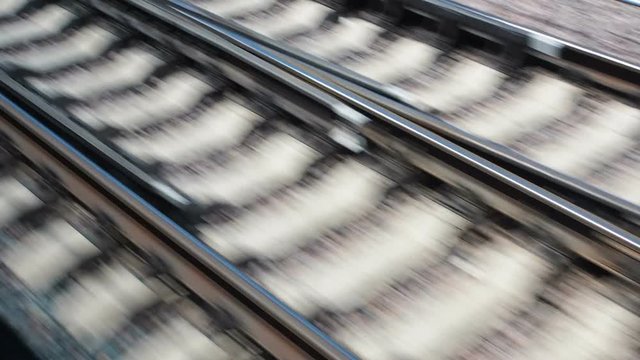 Rails and sleepers flickering during the movement of the train. Angle view of railway from fast train in city from the train window