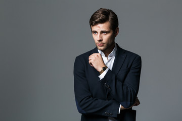 Image of brunette businessman 30s in black jacket looking aside, isolated over gray background