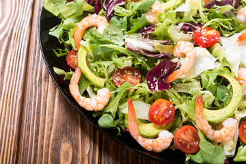 Mix of salad with shrimps , avocado and cherry tomatoes . Healthy food background