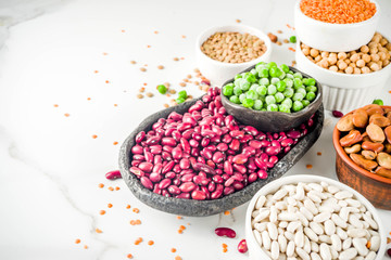 Various assortment of legumes - beans, soy beans, chickpeas, lentils, green peas. Healthy eating concept. Vegetable proteins. White marble background copy space top view