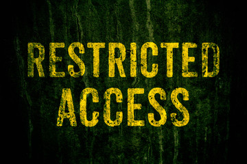 Restricted access warning sign in yellow letters painted over dark grungy cement concrete wall with moss. Sign as concept for: do not enter the area, caution, danger or off limits.