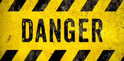 DANGER warning sign word text as stencil with yellow and black stripes painted over concrete wall...