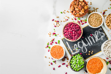 Various assortment of legumes - beans, soy beans, chickpeas, lentils, green peas. Healthy eating concept. Vegetable proteins. White marble background copy space top view