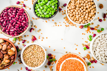 Various assortment of legumes - beans, soy beans, chickpeas, lentils, green peas. Healthy eating concept. Vegetable proteins. White marble background copy space top view