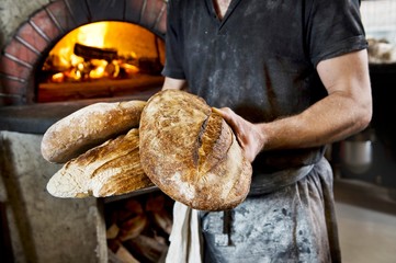 A baker holding several freshly baked wood oven bread loaves in his hands