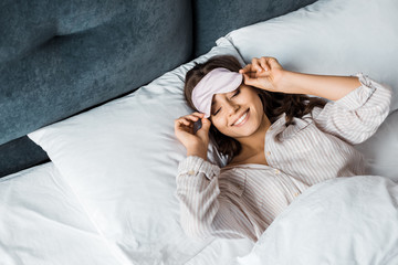 attractive happy girl in sleeping eye mask relaxing in bed in the morning - obrazy, fototapety, plakaty