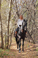 Horseback - woman riding a horse. Horse and equestrian model girl in autumn yellow woods