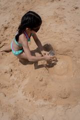 A young girl playing in the sand and building castles. 