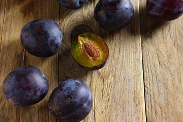 Fresh prune plums, one cut, on wooden surface