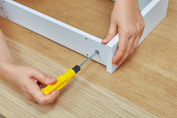 Furniture assembler tightens screw into wooden chipboard drawer.
