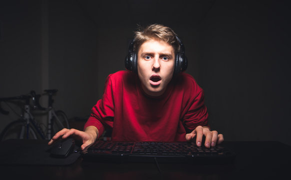 Portrait of a Surprised Gamer for playing video games at home on a computer.Young teen gamer plays home game on his computer. Young man with crystals looks at his computer monitor