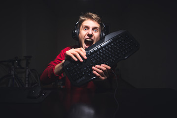 Portrait of an evil gamer playing a video on a computer with a keyboard in his hands and with a...
