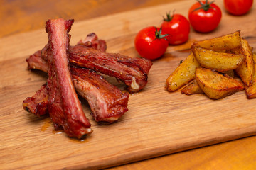 Pork ribs served with tomato and fried potato on wooden table.