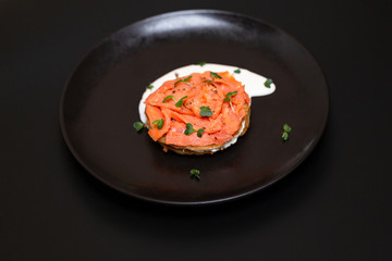Black plate with smoked salmon on a potato pancake with sauce. Tasty snack