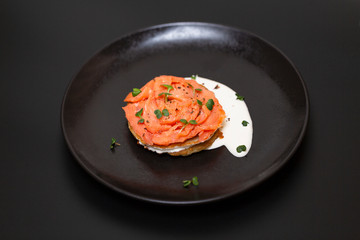 Black plate with smoked salmon on a potato pancake with sauce. Tasty snack