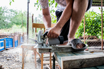 A man works with his hands and a construction tool. Electric saw. Work on wooden boards. To cut the materials. Fine shavings flying in all directions.