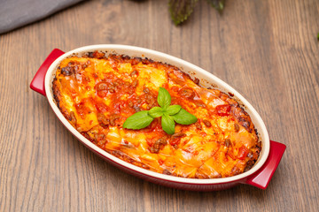 Italian food. Hot tasty freshly baked lasagna served with basil herb on wooden table.