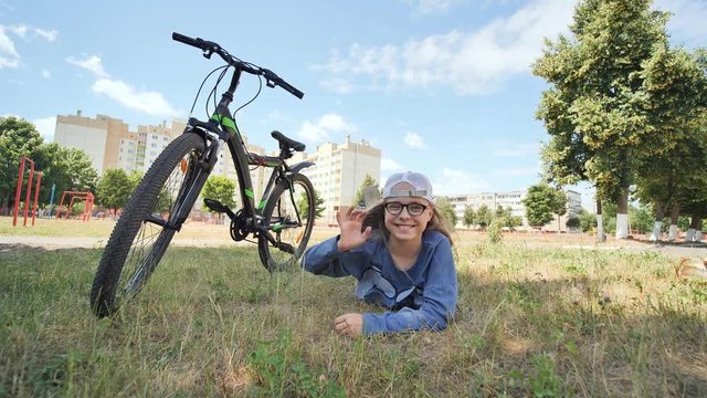 12 year old girl lying on the grass next to her bike and waving her hand