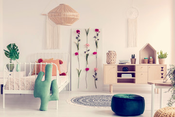 Flower board and cacti shape pillow in boho girl's bedroom interior with natural furniture